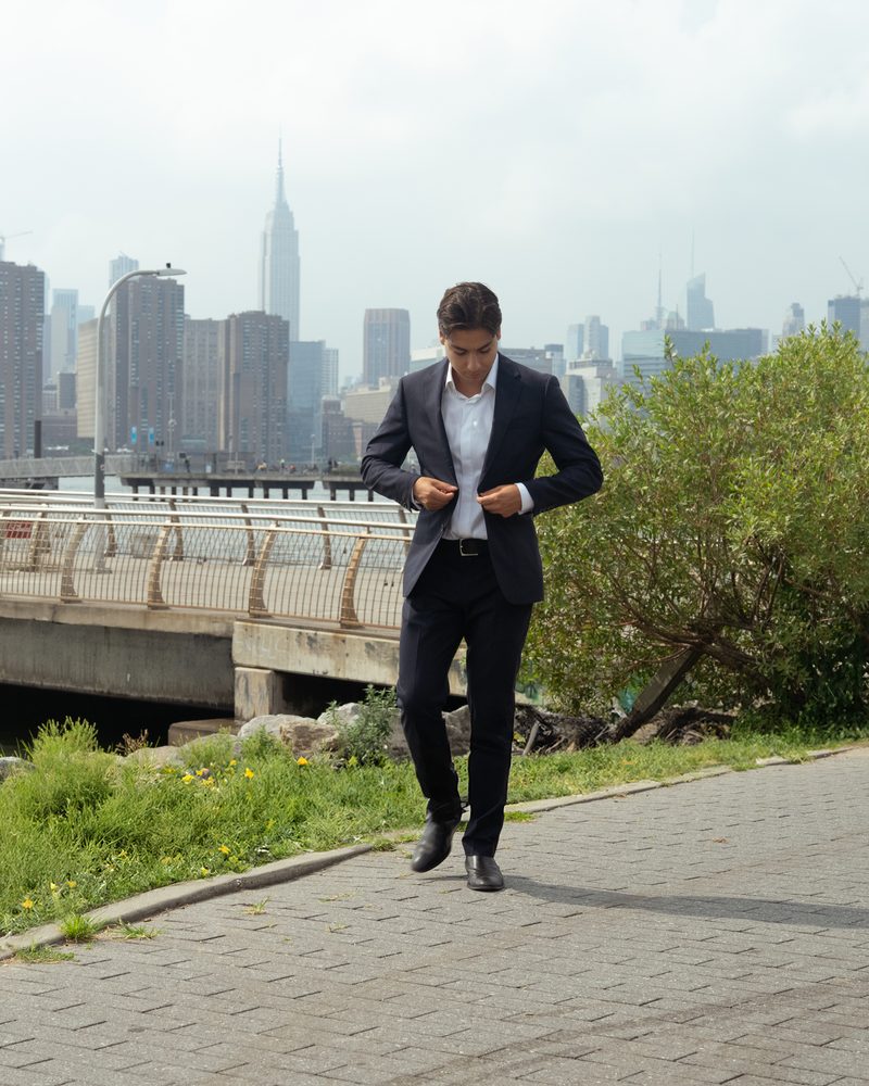 Glenn Velasco walking along the waterfront with the Manhattan skyline behind him